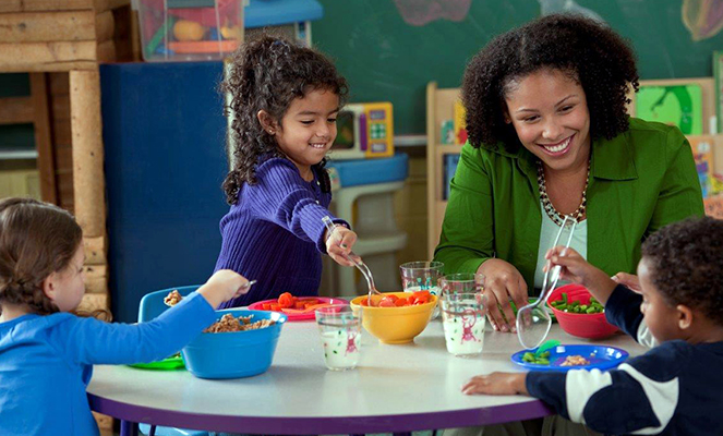 Preschoolers eating family style with assistance from their teacher