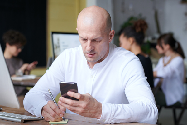 Bald caucasian man on phone at desk.